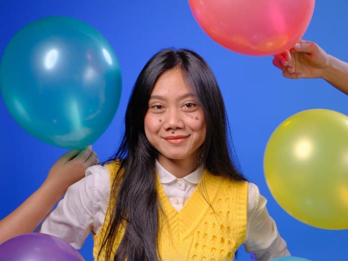 Seorang perempuan tersenyum di antara balon warna-warni