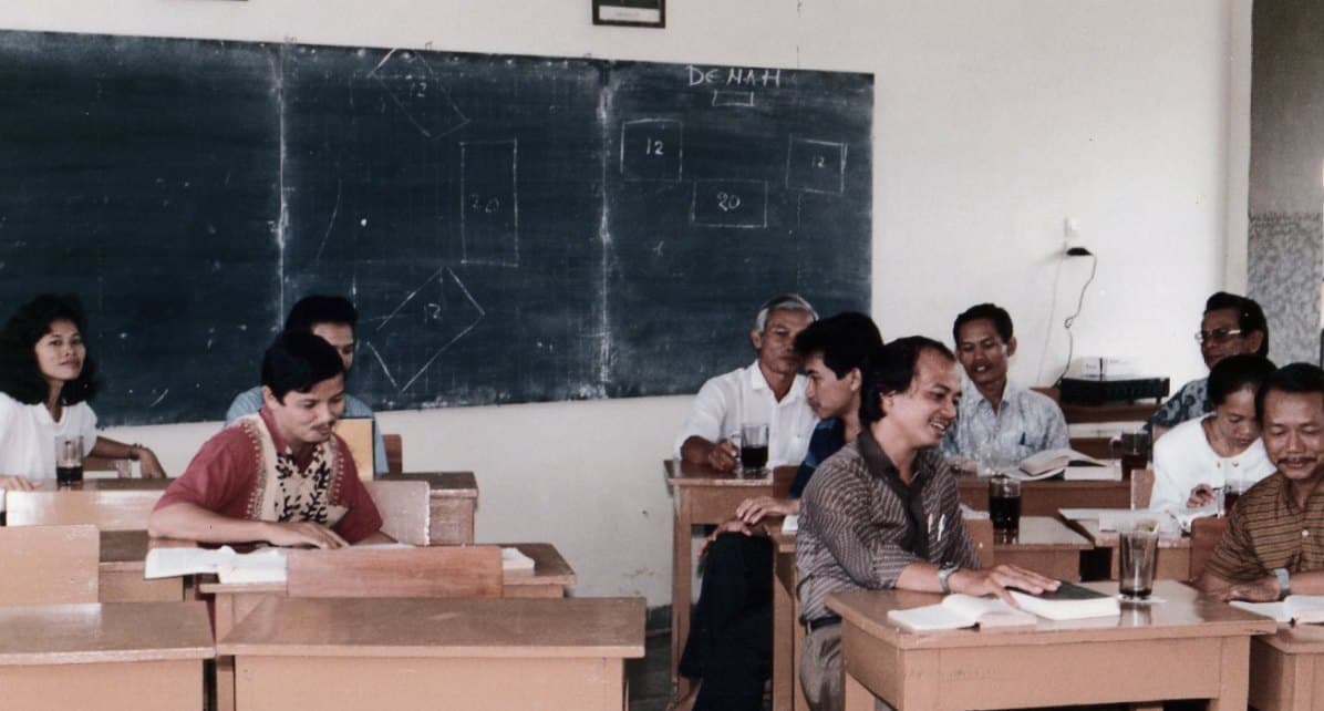 Sekelompok orang duduk di bangku ruang kelas di depan papan tulis